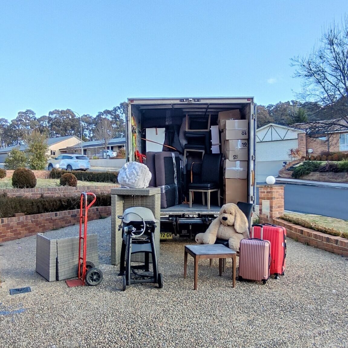 Removal Truck Parked on the Driveway with its rear doors open and loaded with household belongings home furniture appliances etc., some items still on the pavement ready for loading.